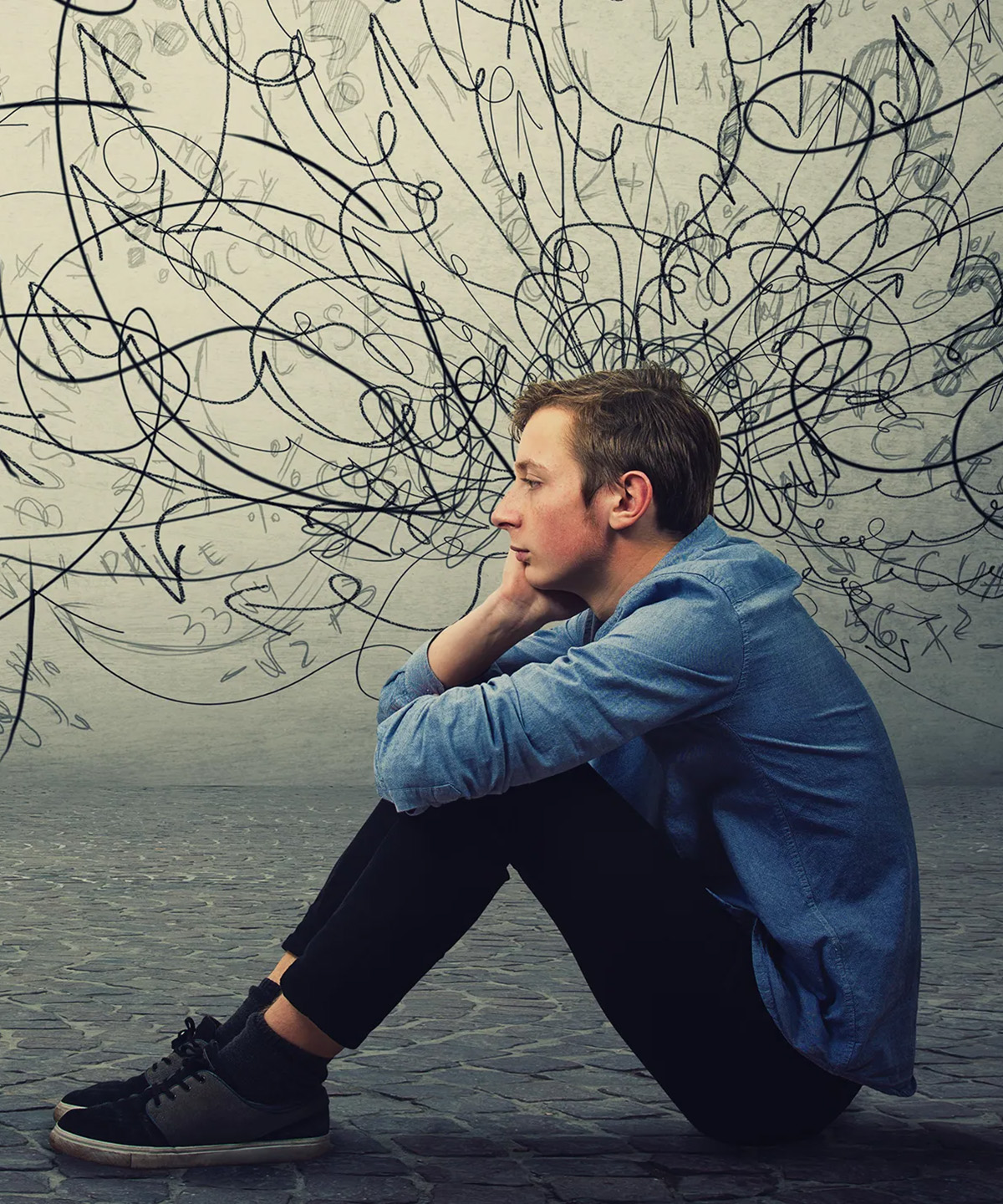 Young man sitting with his head in his hand, surrounded by a tangle of scribbled thoughts